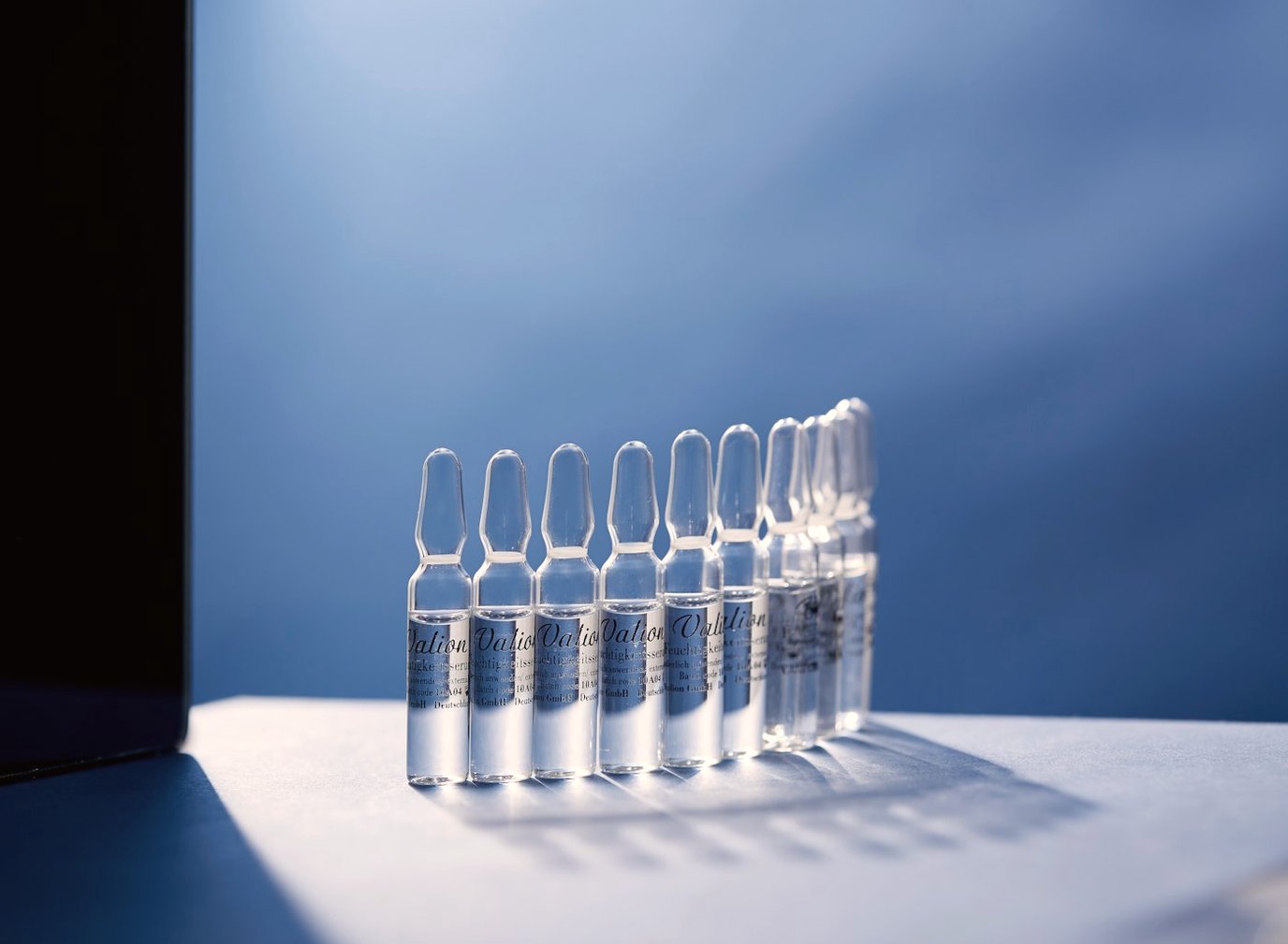 Row of sealed clear glass ampoules standing on a lit surface against a deep blue background.