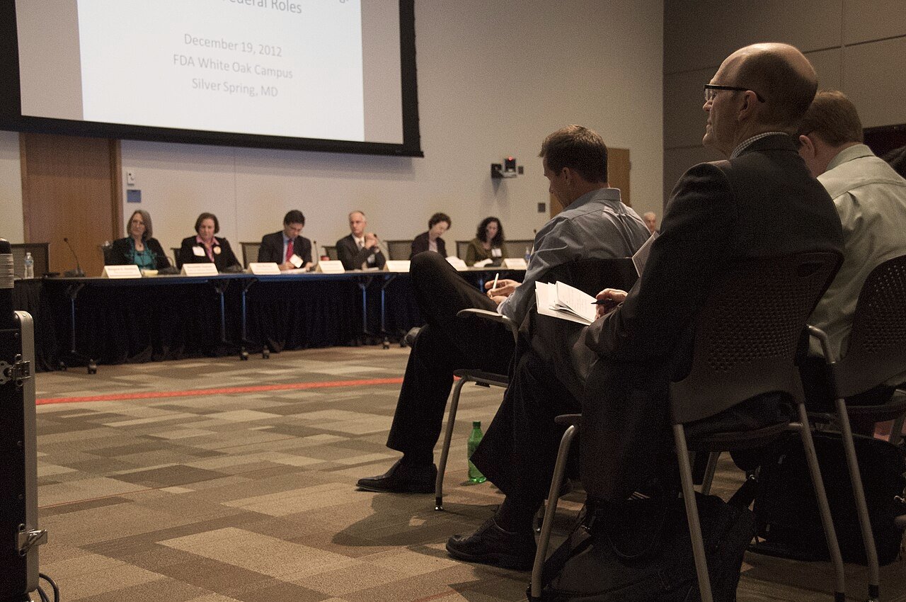 FDA Pharmacy Compounding Advisory Committee seated at a long table in a meeting room at the agency's White Oak campus, projection screen behind them.
