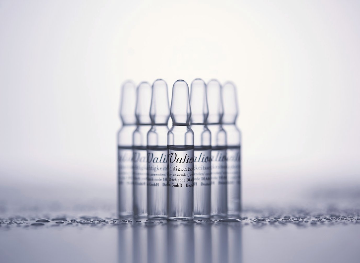 Pale, softly lit row of small labelled glass vials receding into a white background.