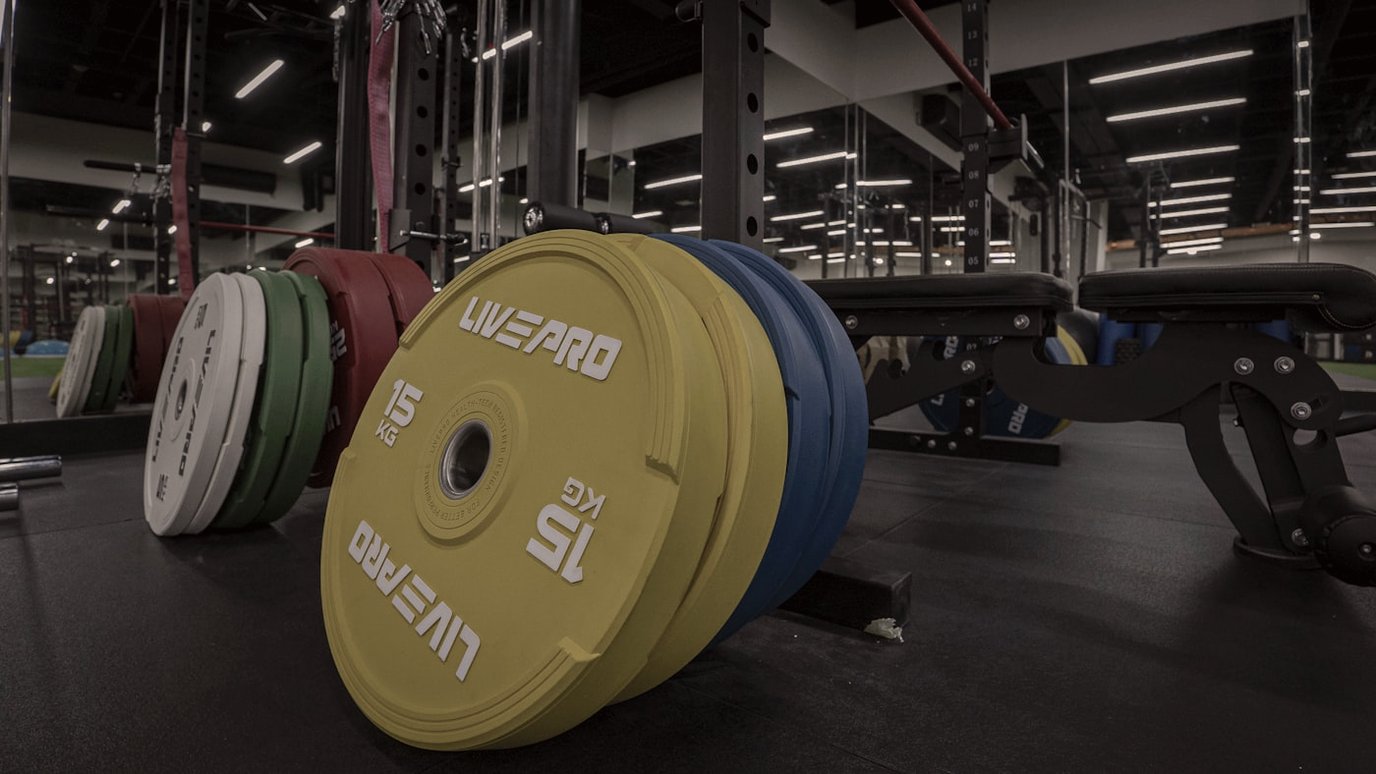 Stacked colour-coded bumper weight plates leaning against a rack on a gym floor.